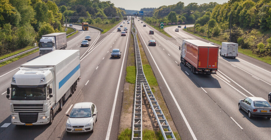 A four lane highway with trucks and passenger cars on both sides.