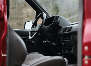 The front interior of a red road vehicle, including center console, steering wheel and passenger's seat.