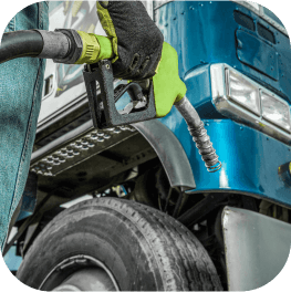 A technician wearing gloves, holding a green fuel nozzle standing next to a large freight vehicle.