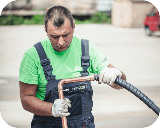 A Mapon technician wearing a green t-shirt, overalls with Mapon logo and white gloves, installing a fuel tracking system.
