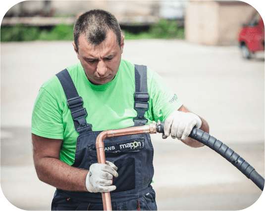 Mapon autoelektriķis, tērpies zaļā kreklā, kombinzonā ar Mapon logo un baltos cimdos, uzstāda degvielas kontroles sistēmu.