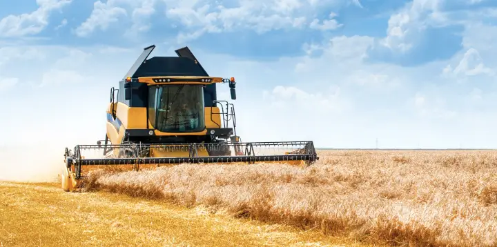 Fleet management in agriculture – a combine harvester transfers grain to a tractor trailer in a wheat field during harvest.
