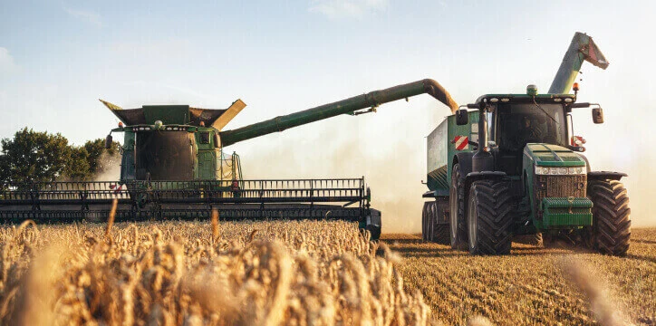 Fleet management in agriculture – a combine harvester transfers grain to a tractor trailer in a wheat field during harvest.