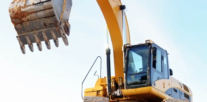 Construction fleet management – a yellow backhoe loader moves gravel at a worksite with trees in the background.