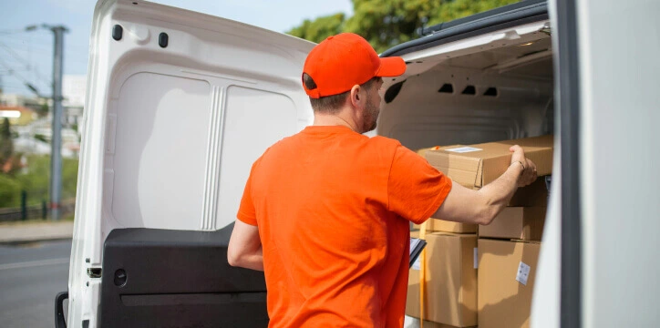 Fleet management for courier services – a delivery driver loads parcels into a white van for last-mile logistics.