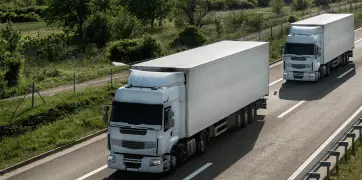 Fleet management in logistics – two long-haul freight trucks driving on a highway through a green landscape.