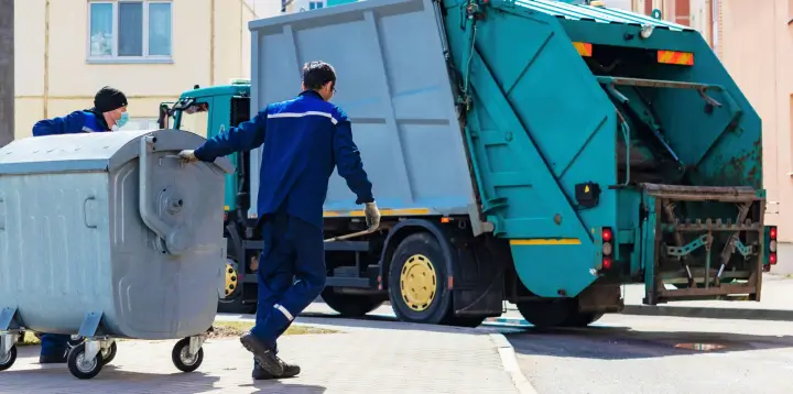 Waste management fleet operations – a garbage truck collects refuse while driving through city streets.