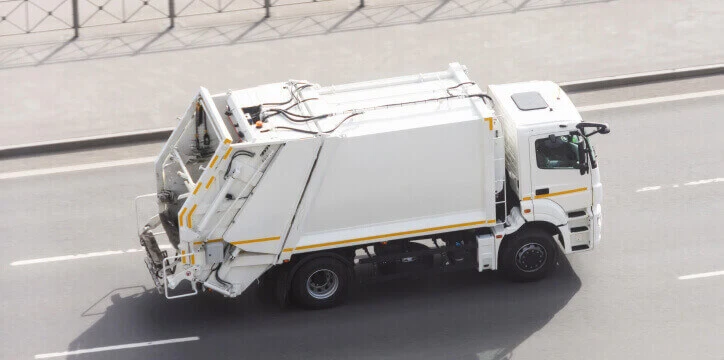 Waste management fleet operations – a garbage truck collects refuse while driving through city streets.