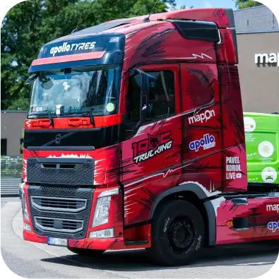 Raudonas „Volvo“ sunkvežimis su „1905 TRUCKING“, „Mapon“ ir „Apollo Tyres“ prekės ženklais, pastatytas šalia „Mapon“ pastato