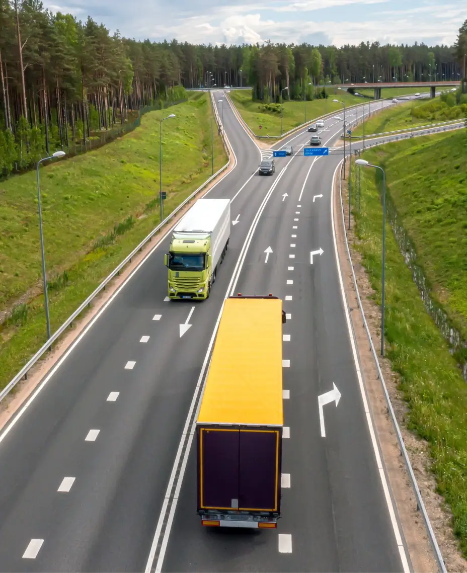 Gul och grön lastbil på en motorväg med skog bredvid.