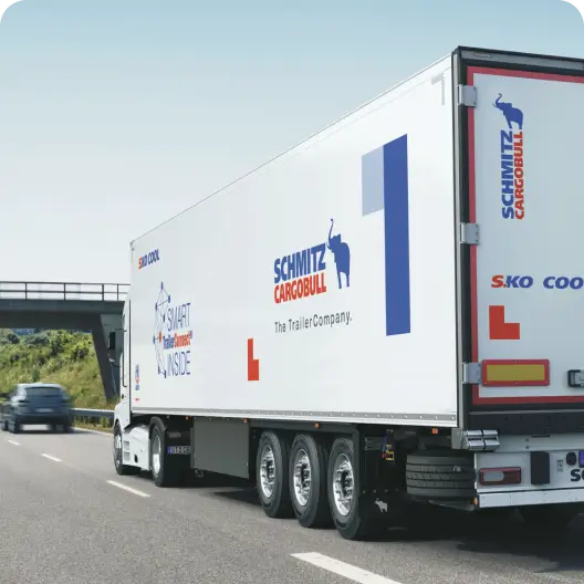 Білий причіп Schmitz Cargobull, який перевозять по шосе.