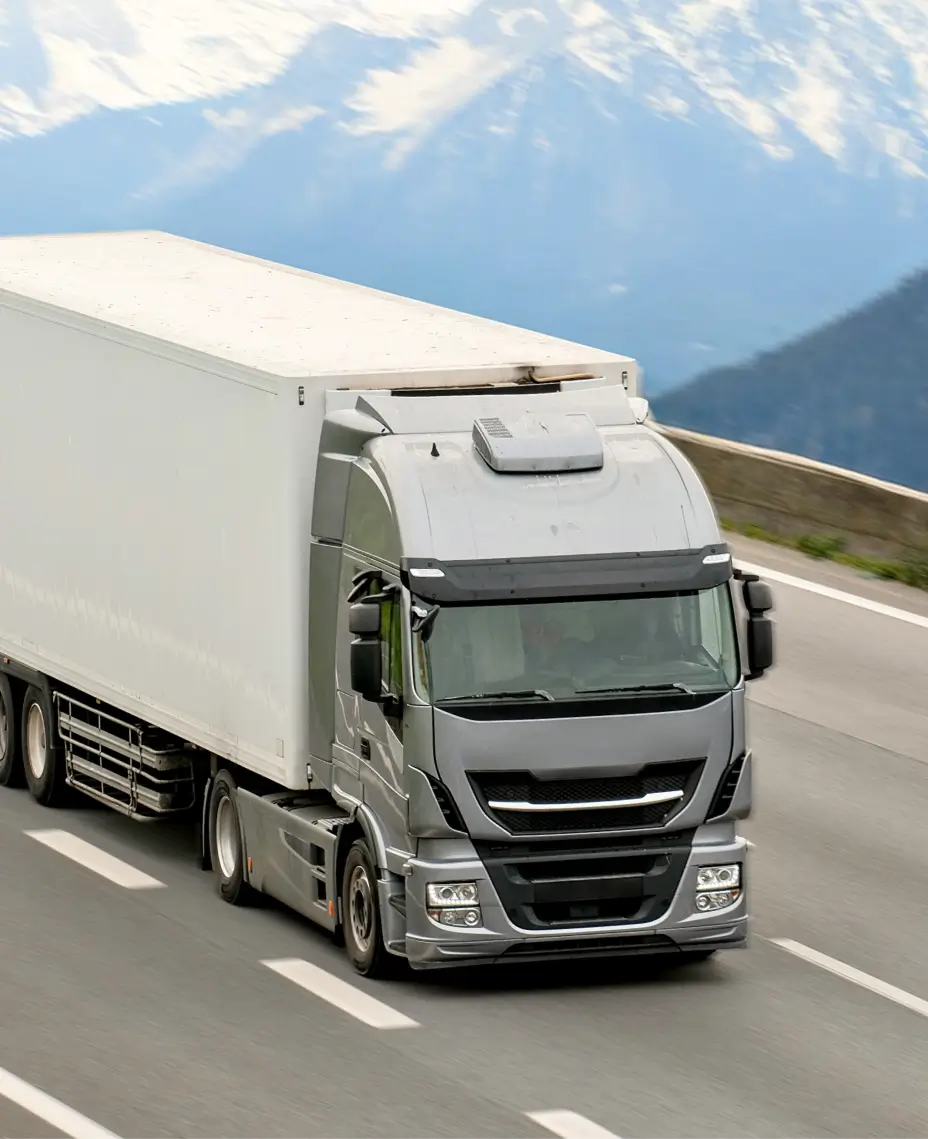 Grey refrigerated truck driving on a highway with mountain scenery in the background.