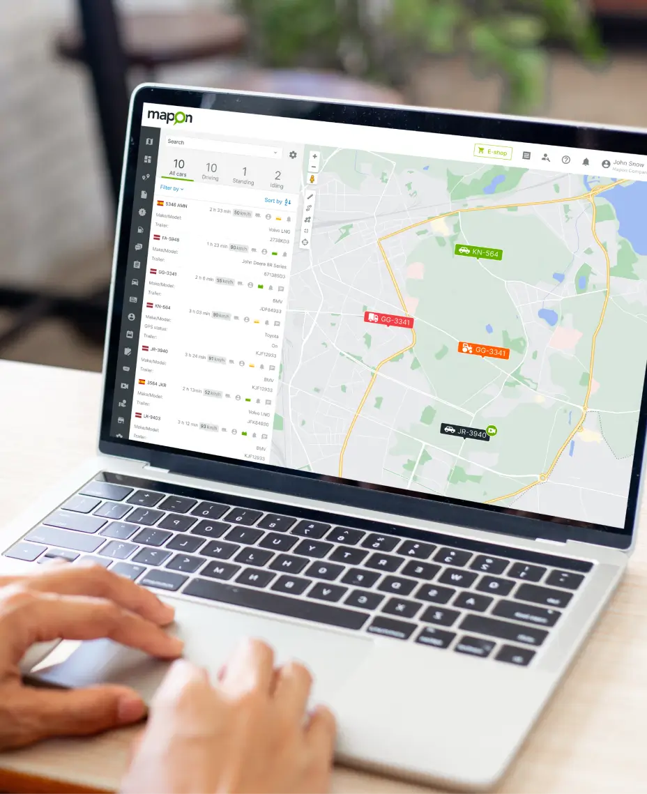 Person using a laptop showing the Mapon fleet tracking dashboard with live vehicle locations.