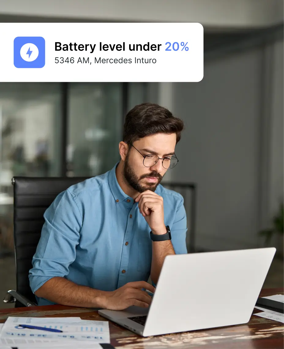 Man working on a laptop with a “Battery level under 20%” alert for a Mercedes Inturo vehicle displayed.