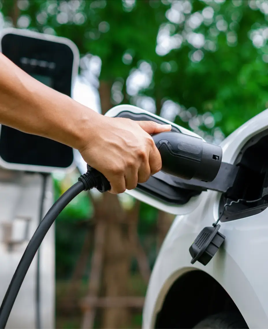 Close-up of a person plugging a charging cable into an electric vehicle at a charging station outdoors.
