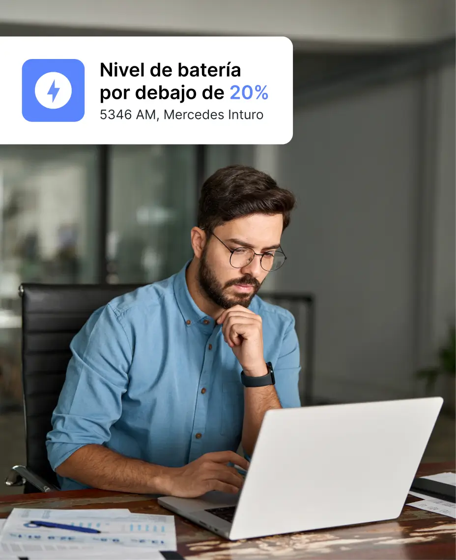 Hombre trabajando en una laptop con una alerta de “Nivel de batería por debajo del 20%” para un vehículo Mercedes Inturo mostrada.