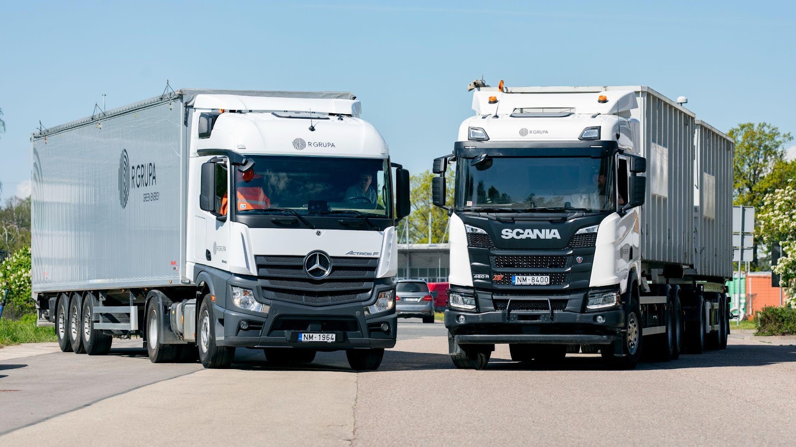 Два белых грузовика с логотипами R GRUP стоят на дороге под углом друг к другу.