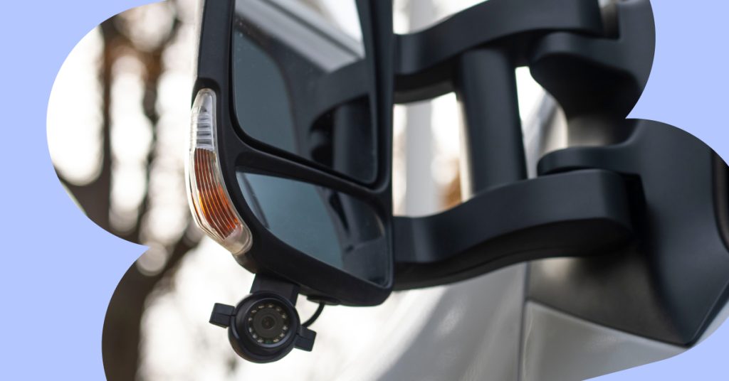 A small side camera installed under a rear-view window of a delivery van.